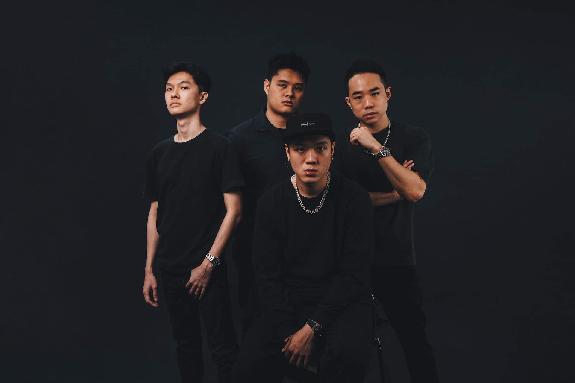 Four individuals of Asian descent standing together against a dark background.
